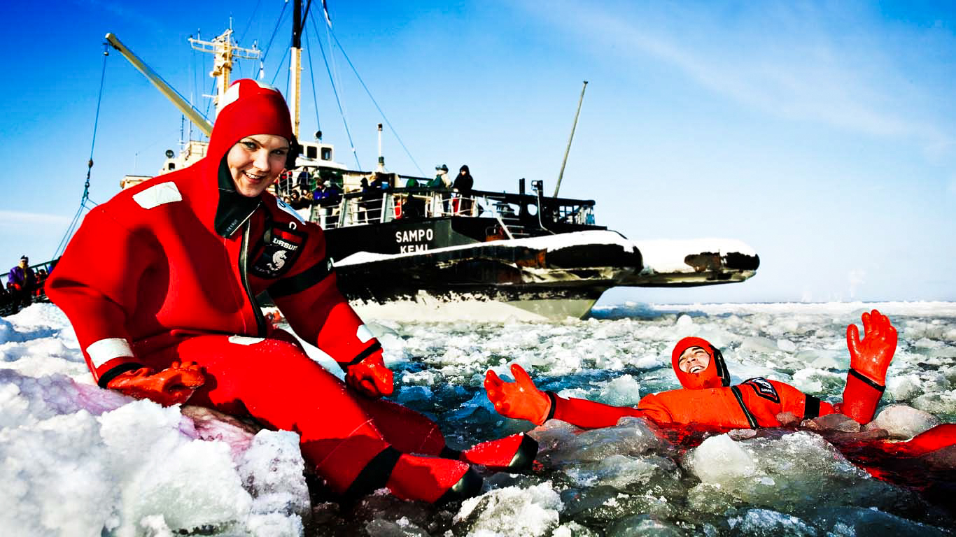 two people in survival suits in ice water in front of ice breaker